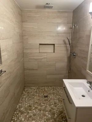 Walk-in shower with beige tile and a pebble floor, by DreamPro Contracting