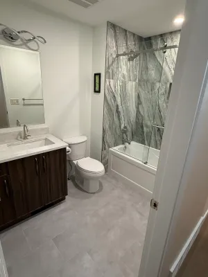 Finished bathroom with a dark wood vanity and a marble-look tiled tub surround, by DreamPro Contracting