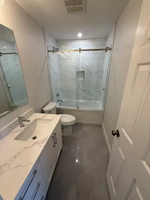 Tub and shower with a marble-look tile surround and a sliding glass door, by DreamPro Contracting