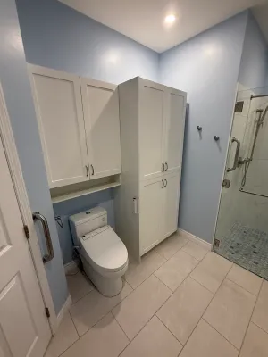 Bathroom with tall white storage cabinets, a blue wall, and a glass shower with a tiled floor, by DreamPro Contracting