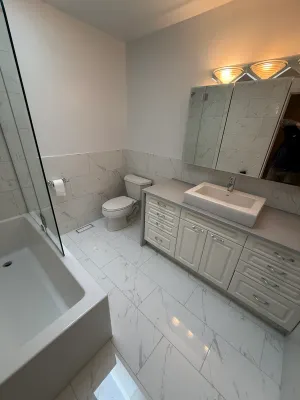 Bathroom with marble-look floor and wall tile, a white vanity, and a glass shower panel, by DreamPro Contracting
