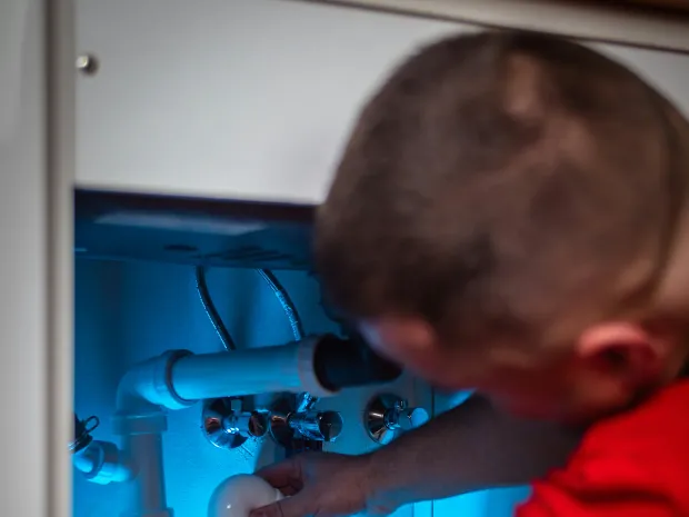A plumber working on the trap under a sink