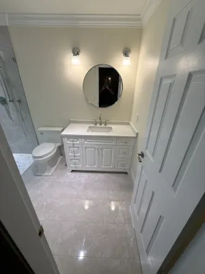 Ensuite with a white vanity, a round mirror, wall sconces, and new floor tile in South Surrey, by DreamPro Contracting
