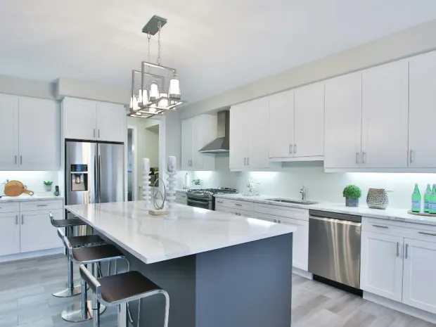 Finished kitchen with white shaker cabinetry, a waterfall quartz island, and a continuous stone backsplash, built by DreamPro Contracting