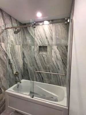 Finished bathroom with a marble-look tiled tub surround and glass panel
