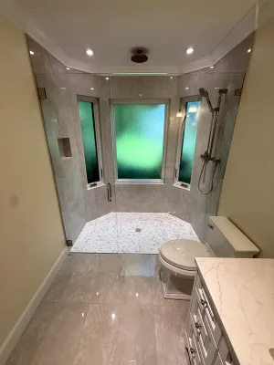 Walk-in shower built into a bay window, tiled floor to ceiling behind a glass door, by DreamPro Contracting