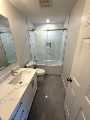 Tub and shower with a marble-look tile surround and a sliding glass door