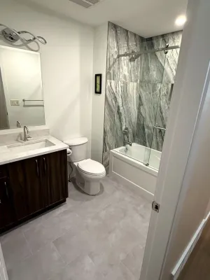 Finished bathroom with a dark wood vanity and marble-look tiled tub surround