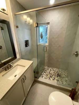 Walk-in shower with frameless glass, textured wall tile, and a pebble floor