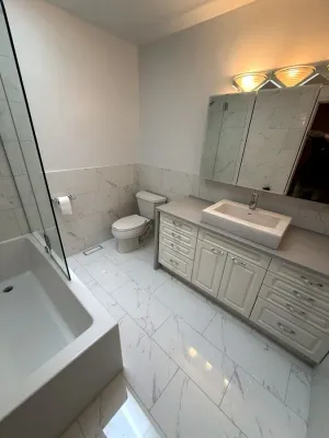 Bathroom with marble-look floor and wall tile, a white vanity, and a glass shower panel