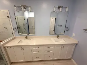 Double vanity with white shaker cabinets, twin mirrors, and a walk-in shower, by DreamPro Contracting