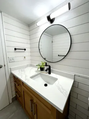Powder room with shiplap walls, a wood vanity, and a round black mirror