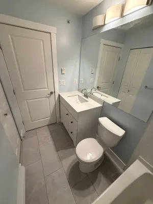 Renovated bathroom with a white vanity, grey large-format floor tile, and a white-tiled tub surround, by DreamPro Contracting