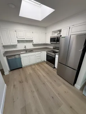 Finished kitchen with white shaker cabinets, grey quartz counters, and stainless appliances, by DreamPro Contracting
