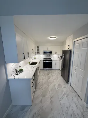 Finished kitchen with white cabinets, veined quartz counters, and a blue accent wall, by DreamPro Contracting