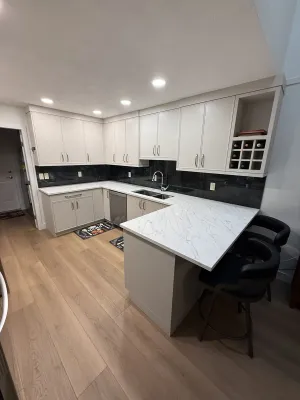 Finished kitchen with white cabinets, a black backsplash, and a marble-look island with seating, by DreamPro Contracting