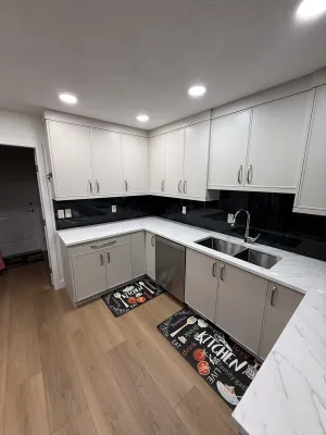 Finished kitchen with white cabinets, a black backsplash, and an undermount double sink, by DreamPro Contracting