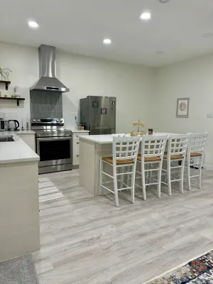 Finished kitchen with a white shaker island, bar stools, and a stainless range hood, by DreamPro Contracting