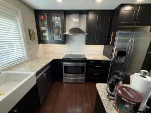 Finished kitchen with black cabinets, glass-front uppers, a subway-tile backsplash, and granite counters, by DreamPro Contracting