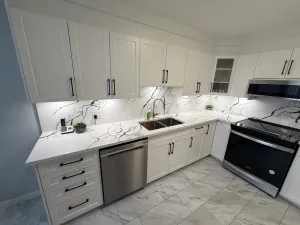 Finished kitchen with white shaker cabinets, a marble-look backsplash, and black hardware, by DreamPro Contracting