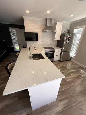 Finished kitchen with a waterfall quartz island and stainless appliances, by DreamPro Contracting