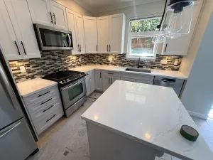 Renovated kitchen with white shaker cabinets, a mosaic tile backsplash, a quartz island, and stainless appliances, by DreamPro Contracting