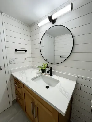 Powder room with shiplap walls, a wood vanity, and a round black mirror, by DreamPro Contracting