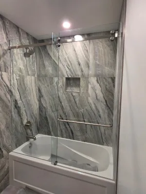 Finished bathroom with a marble-look tiled tub surround and a glass panel, by DreamPro Contracting